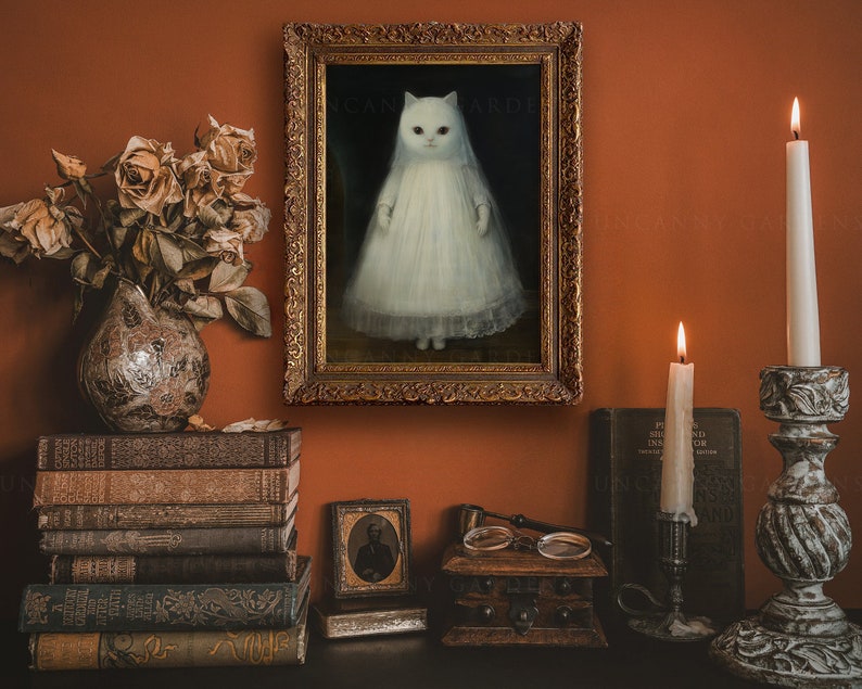 May include: A framed painting of a white cat wearing a white dress, hanging on a wall with a dark orange background. The painting is surrounded by books, candles, and a small wooden box.