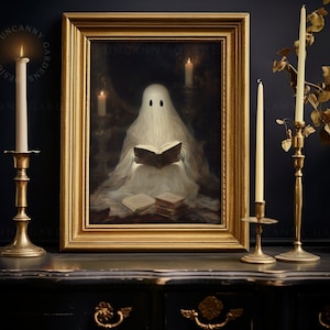 May include: A framed painting of a white ghost reading a book in a dimly lit room with candles. The painting is in a gold frame and is on a black surface with two gold candle holders.