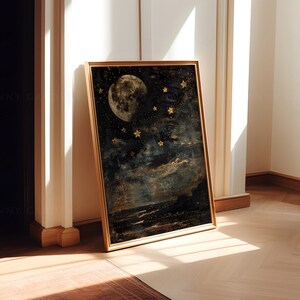 May include: A framed print of a moon and stars in a dark blue and gold color scheme. The moon is full and has a textured surface. The stars are scattered across the sky and are a bright gold color.