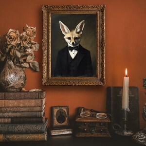 May include: An antique-style framed portrait of a fox in a tuxedo hangs on a burnt orange wall. The scene includes a vase of dried roses, stacked vintage books, lit candles, and decorative candle holders, creating a vintage aesthetic.