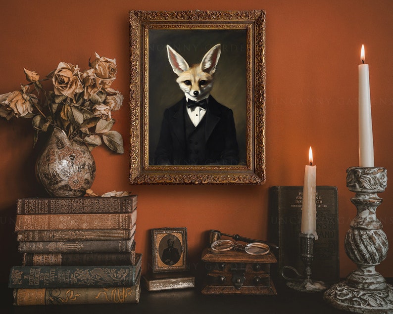 May include: An antique-style framed portrait of a fox in a tuxedo hangs on a burnt orange wall. The scene includes a vase of dried roses, stacked vintage books, lit candles, and decorative candle holders, creating a vintage aesthetic.