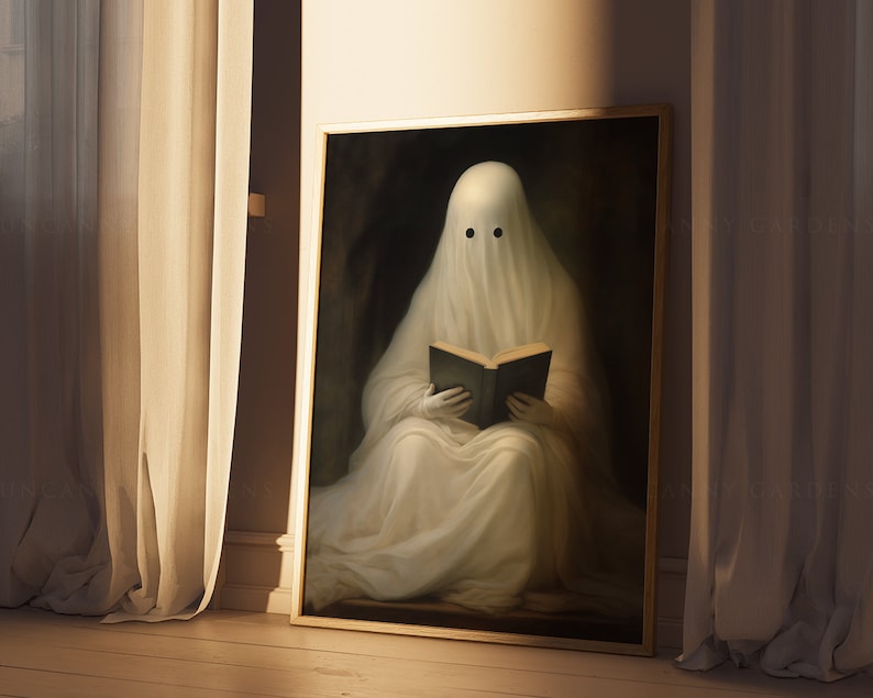May include: A framed print depicts a ghost reading a book. The ghost is draped in a white sheet with two black eye holes. The artwork has a dark, moody background and is framed in gold. The image is set against a backdrop of beige curtains and a wooden floor.