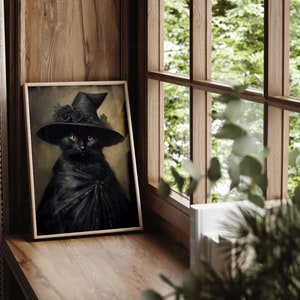 May include: A black cat wearing a witch's hat with black roses and a black cape. The cat is looking directly at the viewer. The image is framed in a wooden frame.