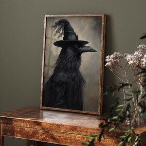 以下が含まれることがあります： 魔女の帽子をかぶった黒いカラスの絵画が額装されています。カラスは、リアルなスタイルで、羽根が細かく描かれ、真剣な表情をしています。背景は、柔らかく落ち着いた茶色です。