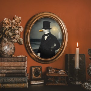 May include: A framed portrait of a seagull wearing a black top hat and a bow tie. The portrait is set against a backdrop of a seascape. The portrait is hanging on a wall with a stack of books, a small framed picture, and two candlesticks with lit candles on either side.
