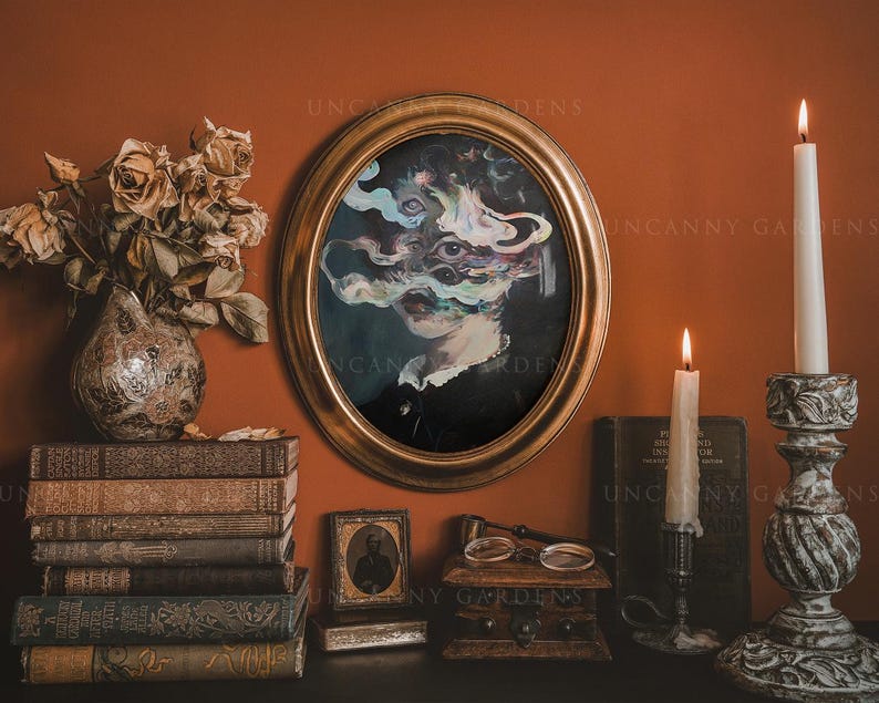 May include: An oval framed portrait with a surreal face, surrounded by candles, books, and a vase of dried flowers. The painting features a woman's face with multiple eyes and colorful smoke-like elements. The scene is set against a warm orange wall.