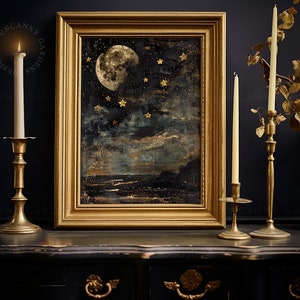May include: A framed painting of a moon and stars in a dark blue sky with gold accents. The painting is on a black table with two gold candle holders and candles.