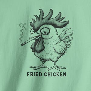 May include: A light green t-shirt featuring a black and white illustration of a chicken smoking a cigarette. The chicken has a grumpy expression. The words "FRIED CHICKEN" are printed below the chicken.