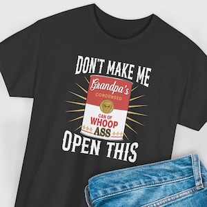May include: Black t-shirt with the text "DON'T MAKE ME OPEN THIS" above a graphic of a can labeled "Grandpa's Condensed Can of Whoop Ass". The can is red and white with a gold emblem.