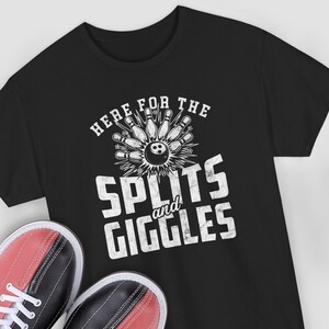 Può includere: T-shirt nero con grafica a tema bowling. Il design presenta una palla e birilli da bowling con la scritta "HERE FOR THE SPLITS and GIGGLES" in bianco. Scarpe da bowling rosse e nere in basso.