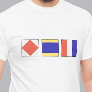 Peut inclure: Un t-shirt blanc à manches courtes orné de trois drapeaux de signalisation maritime carrés imprimés en ligne horizontale sur la poitrine. Le premier est blanc avec un losange rouge, le deuxième est jaune et bleu, et le troisième est rouge, blanc et bleu.