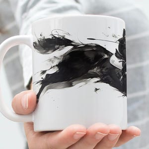 以下が含まれることがあります： 白のセラミックマグカップ。黒と白のインクで描かれた馬と騎手のイラストが特徴です。このアートワークは、流れるような筆致でダイナミックなシーンを描き、動きの感覚を生み出しています。マグカップには湾曲したハンドルが付いています。
