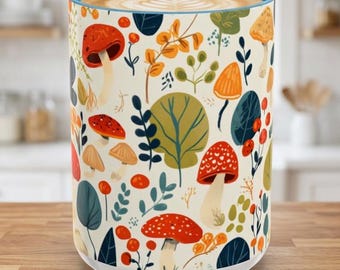 May include: A ceramic mug with a cream-colored background featuring a repeating pattern of various mushrooms, berries, and foliage in shades of red, orange, green, and blue. The mug has a light blue rim and contains a beverage with latte art.
