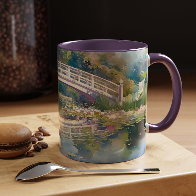 May include: A ceramic mug with a purple interior and handle, featuring a colorful watercolor-style print of a white arched bridge over a pond with water lilies and lush green foliage, reflecting the scene on the water surface below.