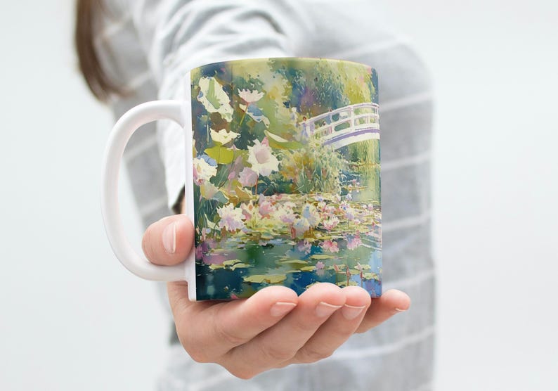 May include: A white ceramic mug featuring a colorful impressionist-style painting of a water lily pond with a small arched bridge. The artwork displays vibrant shades of green, blue, pink, and white, depicting aquatic plants and reflections.