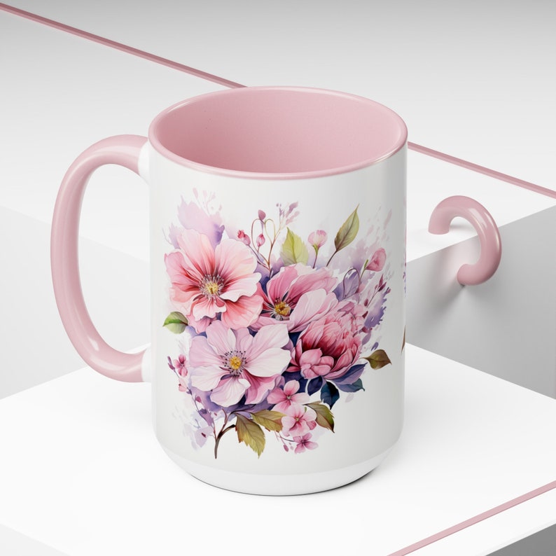 Puede incluir: Una taza de cer&aacute;mica rosa con un dise&ntilde;o floral blanco con flores rosas, moradas y verdes. La taza tiene un asa rosa.
