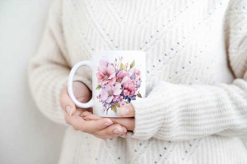 Puede incluir: Taza de cer&aacute;mica blanca con un dise&ntilde;o floral con flores rosas, moradas y blancas. La taza tiene un asa y la est&aacute; sujetando una persona.