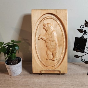 May include: A wooden wall plaque with a carved bear in an oval frame. The bear is standing on its hind legs and has a detailed, textured design.