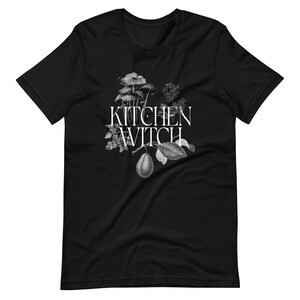 May include: Black t-shirt with a white graphic of a pear, mushrooms, and leaves with the text "Kitchen Witch" in white.