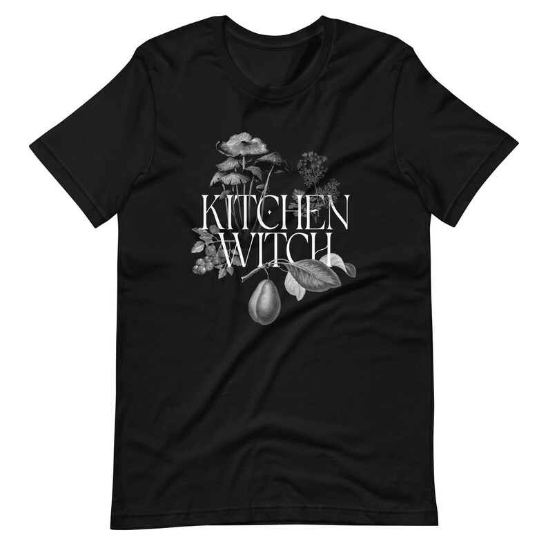 May include: Black t-shirt with a white graphic of a pear, mushrooms, and leaves with the text "Kitchen Witch" in white.