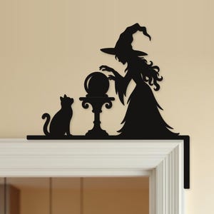 May include: A black silhouette wall decal designed to fit on a door frame corner. The design features a witch wearing a pointed hat, standing beside a pedestal with a crystal ball, and a cat sitting on the other side of the pedestal.