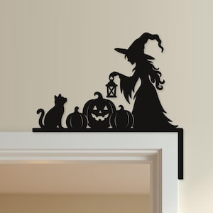 May include: A black metal door corner sign featuring a silhouette of a witch wearing a pointed hat and holding a lantern, accompanied by a cat and three pumpkins, designed to fit onto the top corner of a door frame for decorative display.