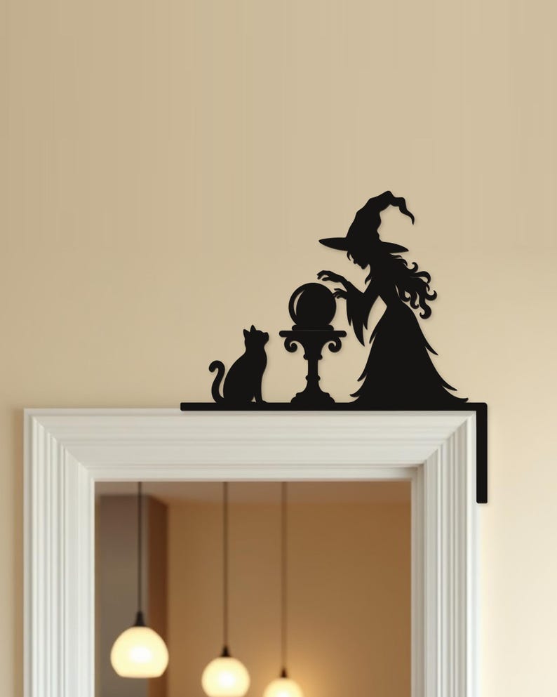 May include: A black silhouette wall decal designed to fit on a door frame corner. The design features a witch wearing a pointed hat, standing beside a pedestal with a crystal ball, and a cat sitting on the other side of the pedestal.