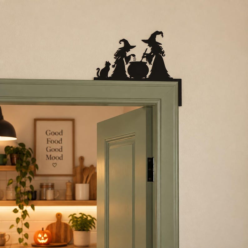 May include: A black metal door corner sign featuring a silhouette of two witches wearing pointed hats, standing beside a cauldron and a cat. The decorative piece is designed to be mounted on the upper corner of a door frame for display.