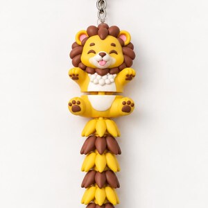 May include: A keychain featuring a cartoon lion with a yellow body, brown mane, and a long, articulated tail made of alternating yellow and brown segments. The lion has a smiling expression with its tongue out and is attached to a silver metal ring.
