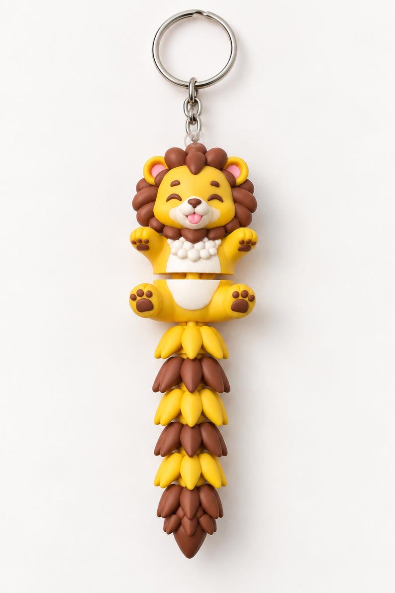 May include: A keychain featuring a cartoon lion with a yellow body, brown mane, and a long, articulated tail made of alternating yellow and brown segments. The lion has a smiling expression with its tongue out and is attached to a silver metal ring.