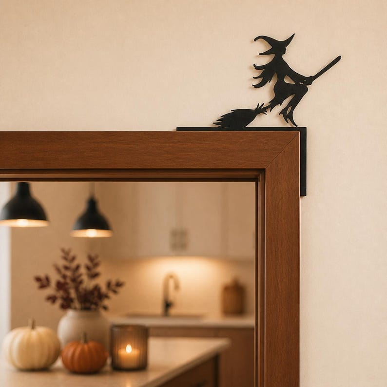 May include: A black metal silhouette of a witch riding a broomstick, designed to be mounted on the corner of a door frame. The flat, cutout figure depicts a pointed hat, flowing hair, and a broom, positioned to sit flush against the wooden trim.