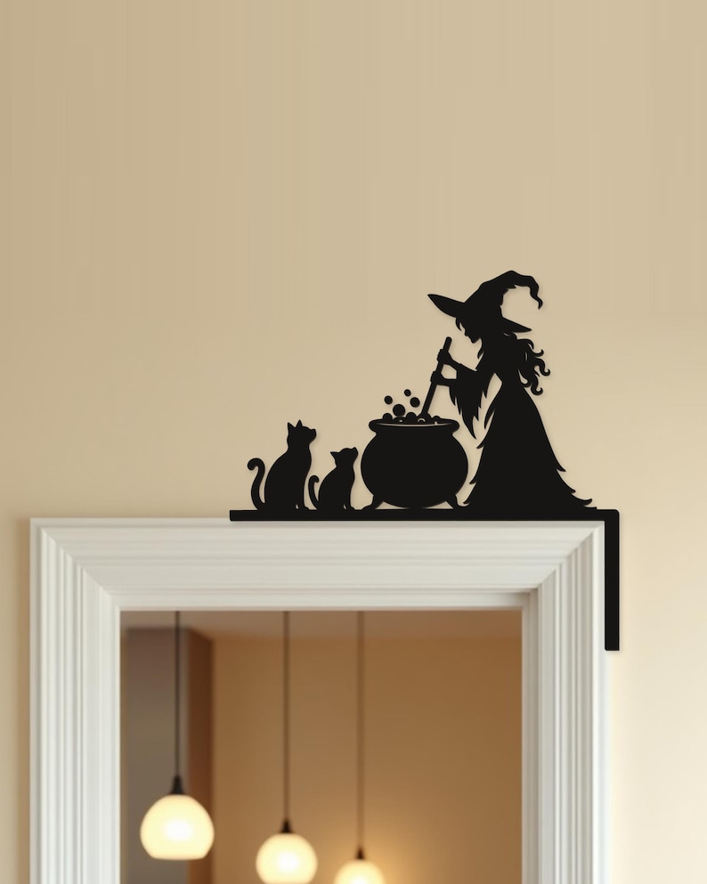 May include: A black metal door corner topper featuring a silhouette of a witch wearing a pointed hat, standing beside a bubbling cauldron and stirring it with a long spoon, accompanied by two cats sitting side by side on a flat horizontal base.