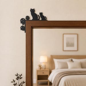May include: A black metal door corner accent piece featuring silhouettes of two cats and three ghosts. The decorative item is designed to be mounted on the upper corner of a door frame, showcasing a flat, solid black finish with distinct shapes.