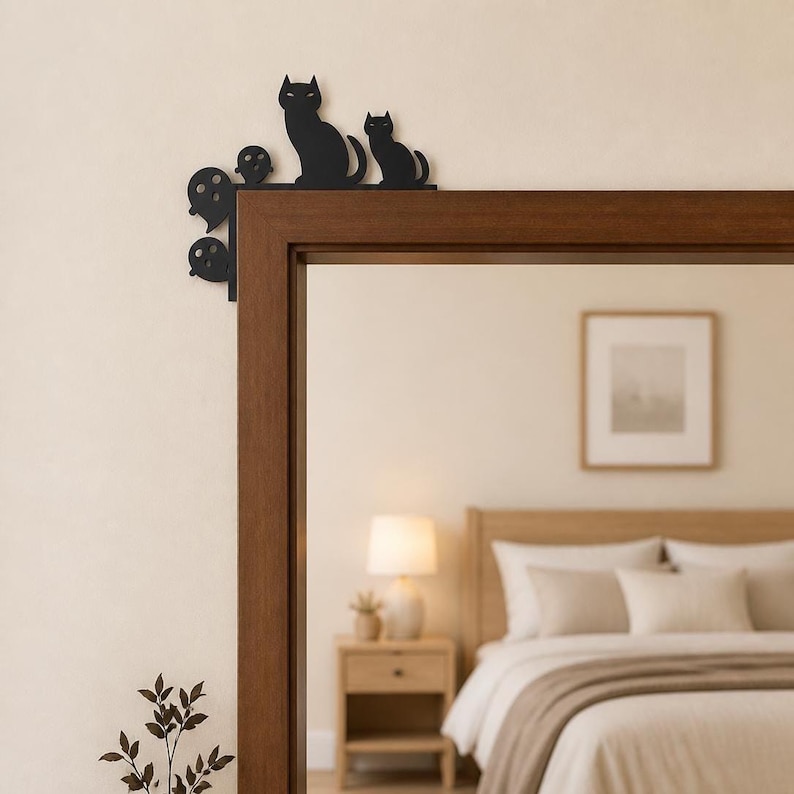 May include: A black metal door corner accent piece featuring silhouettes of two cats and three ghosts. The decorative item is designed to be mounted on the upper corner of a door frame, showcasing a flat, solid black finish with distinct shapes.