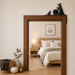 May include: A black metal door corner sign featuring a silhouette of a witch wearing a pointed hat, standing next to a cauldron and a cat. The decorative piece is designed to be mounted on the top corner of a door frame as a wall accent.