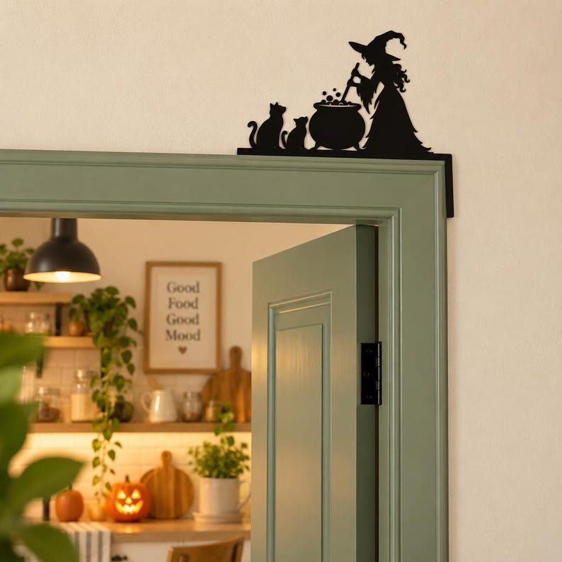 May include: A black metal door corner sign featuring a silhouette of a witch wearing a pointed hat, standing beside a bubbling cauldron and two cats. The decorative piece is designed to be mounted on the top corner of a door frame.