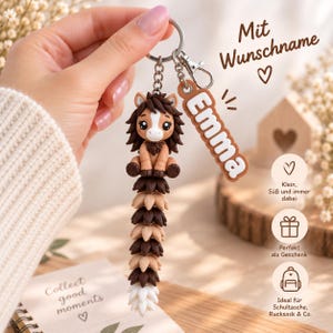 May include: A keychain featuring a brown and tan horse figurine with a long, segmented tail made of alternating dark brown, light brown, and white pieces. A separate rectangular brown tag with the white text Emma is attached to the metal ring.