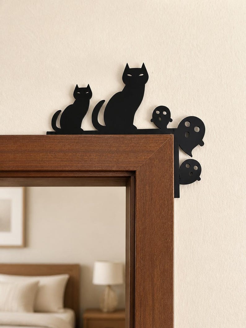 May include: A black metal door corner decoration featuring a silhouette of two cats and three ghosts. The design is shaped to fit over the top corner of a door frame, with the cats positioned along the top edge and the ghosts along the side.