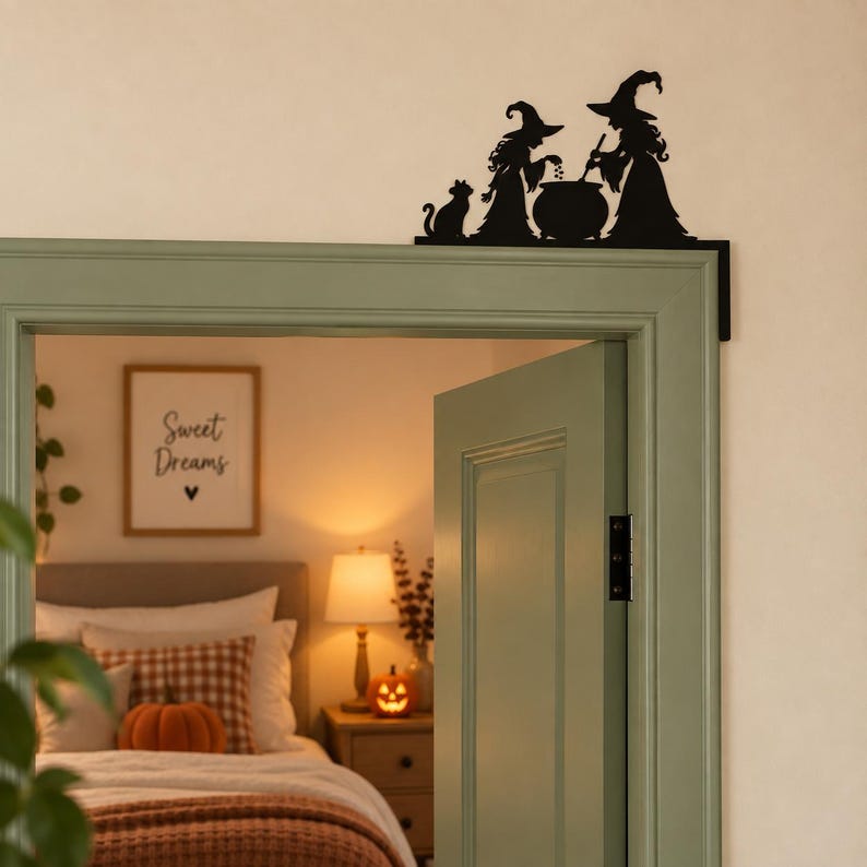 May include: A black metal door corner decoration featuring a silhouette of two witches standing by a cauldron with a cat. The design is shaped to fit into the top corner of a door frame, displaying a detailed scene of figures in pointed hats.