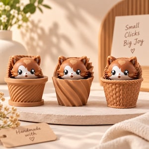 May include: Three small brown and white cat figurines with heart-shaped markings on their foreheads, each nestled in a distinct brown container: a spiral-textured pot, a twisted cup, and a woven basket. A card reads Small Clicks Big Joy.