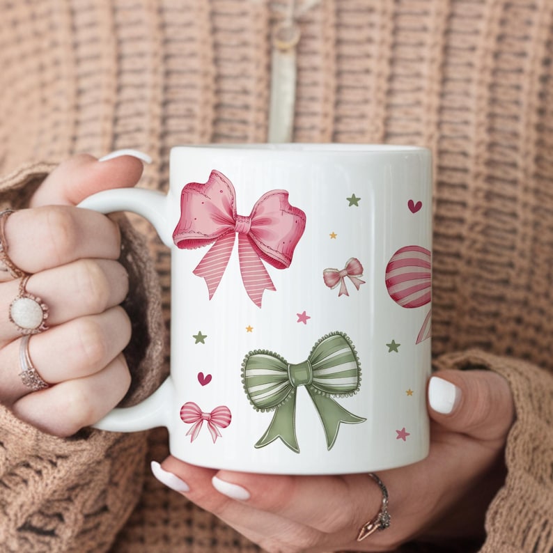 Peut inclure: Une tasse en c&eacute;ramique blanche avec un motif de n&oelig;uds rose et vert. La tasse a une anse et est d&eacute;cor&eacute;e d'&eacute;toiles et de c&oelig;urs.