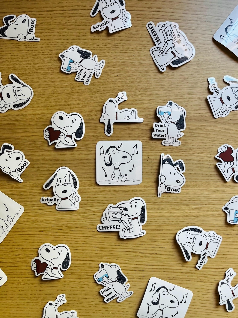 K&ouml;nnte beinhalten: Eine Sammlung von schwarz-wei&szlig;en Aufklebern mit einem Cartoon-Hund mit verschiedenen Ausdr&uuml;cken und S&auml;tzen. Die S&auml;tze lauten "Boo!" "Actually" "Drink Your Water!" "Cheese!" und "222".