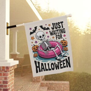 May include: A white Halloween flag with a skeleton relaxing in a pink inner tube, surrounded by pumpkins and stars. The flag reads "JUST WAITING FOR HALLOWEEN" in black text, with bats above.