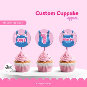 May include: Three cupcakes with pink frosting and sprinkles, topped with custom cupcake toppers. The toppers feature denim overalls designs with text that reads "Can you say? ONE", "1", and "Happy Birthday Marie". The background is pink.