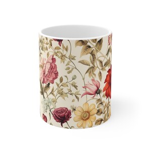 Puede incluir: Taza de cerámica blanca con un estampado floral con flores rosas, rojas y amarillas, y hojas verdes sobre un fondo crema. El diseño envuelve la taza, creando una estética vintage.