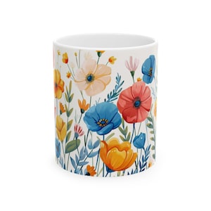 Puede incluir: Taza de cerámica blanca con un diseño floral colorido. Las flores incluyen flores naranjas, amarillas, azules y rosas con hojas verdes. La taza es cilíndrica y tiene un interior blanco.