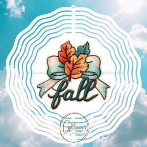 Op de afbeelding: Een decoratieve windspinner met herfstthema met een blauw-witte golvende rand. Het ontwerp toont een blauwgroen lint, kleurrijke herfstbladeren en het woord "fall" in cursief. De achtergrond is een helderblauwe lucht met wolken.