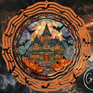 Op de afbeelding: Een Halloween windspinner met een glas-in-lood ontwerp van een spookhuis, pompoenen en vleermuizen. De buitenste rand is oranje met vleermuis silhouetten. De achtergrond toont een stormachtige lucht.
