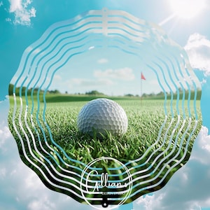 May include: A golf ball rests on green grass on a sunny day, with a red flag in the distance. The image is framed by a white, wavy design against a blue sky with clouds. The logo "Gillian's Design Studio" is at the bottom.