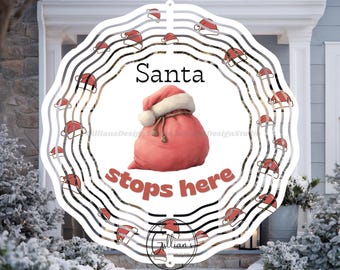 May include: A round, white Christmas decoration with a wavy black and white border. The design features Santa hats and the text "Santa stops here" around a pink Santa bag. The design is set against a snowy outdoor backdrop.